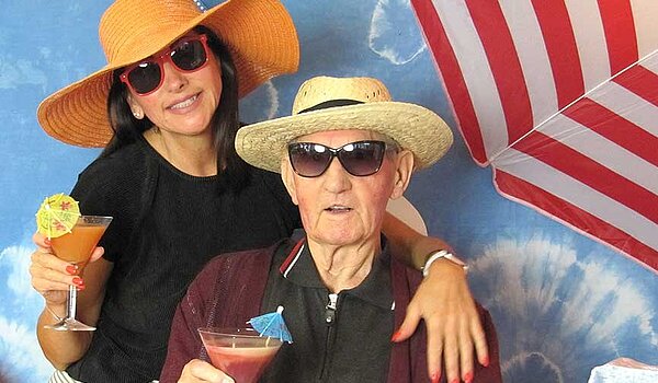 Urlaub in Zeiten von Corona. Senior und Pflegerin mit Fruchtcocktail unterm Sonnenschirm. Urlaub ohne Koffer im Kurhaus Hennef.